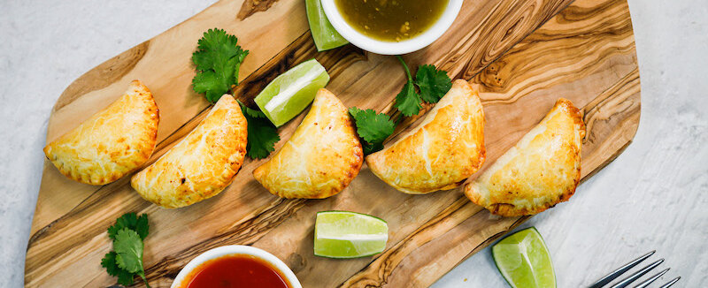 A tray of mini empanadas made with plant-based proteins and a chili-flavored sauce.