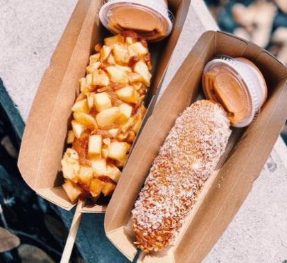 A potato mozzarella corn dog and a mozzarella with sugar corn dog in brown cardboard hot dog holders