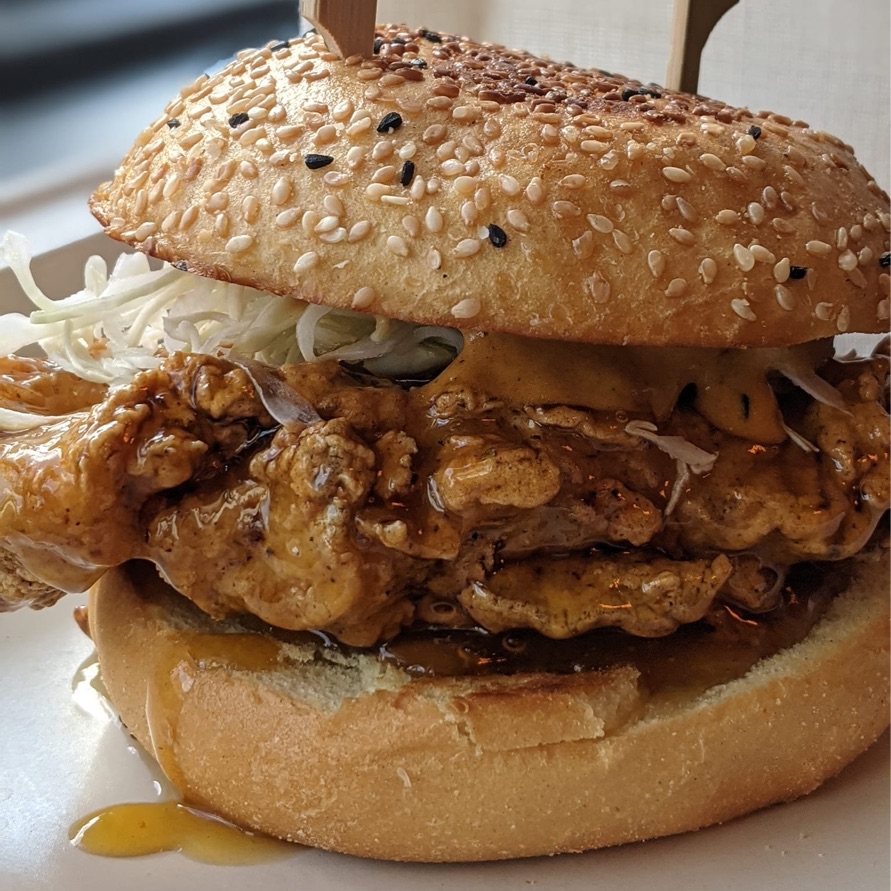 A honey and passion fruit-glazed chicken sandwich with fire-roasted chili mayonnaise and shaved green cabbage on a black and white sesame seed bun.