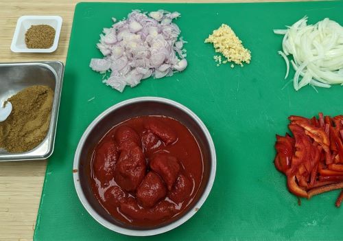 Bowl of tomato sauce, sliced peppers, onions, shallot, and spices on cutting board to make Shakshuka breakfast burritos