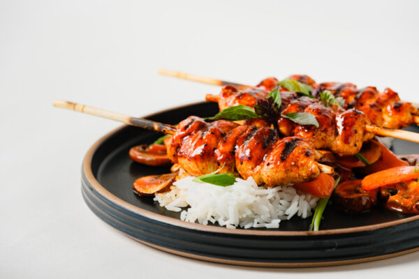 Grilled chicken skewers glazed with a custom-flavored sauce, served over white rice with roasted vegetables.