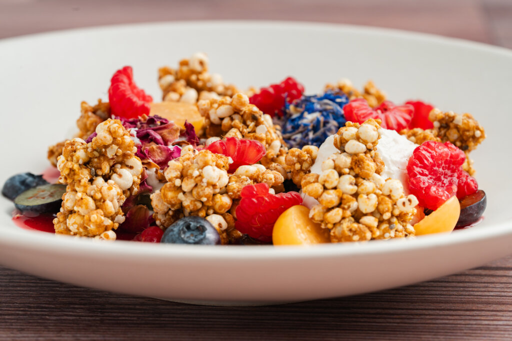 A healthy menu option featuring granola with fresh raspberries, and blueberries, served in a white bowl.