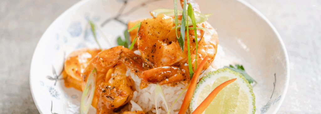 Hot and spicy shrimp over jasmine rice, garnished with lime slices, julienned bell peppers, and green onions – a flavorful dish inspired by international spices like cayenne pepper, black pepper, and ginger, representing bold flavors from around the world.